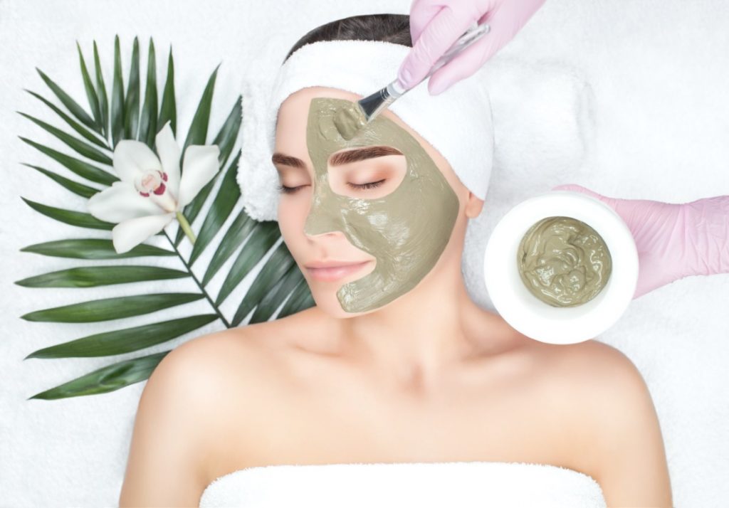 The procedure for applying a mask from clay to the face of a beautiful woman.