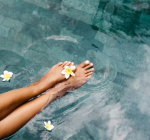 Woman relaxing in swimming pool in Bali luxury resort. Foot spa and skin care lifestyle. Top view photo of legs closeup.