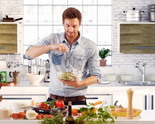 Handsome man cooking at home preparing salad in kitchen.