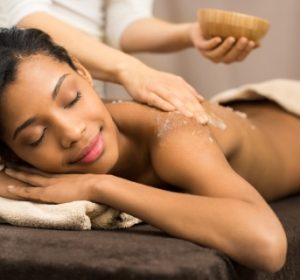 Spa therapist applying scrub salt on young woman back at salon spa